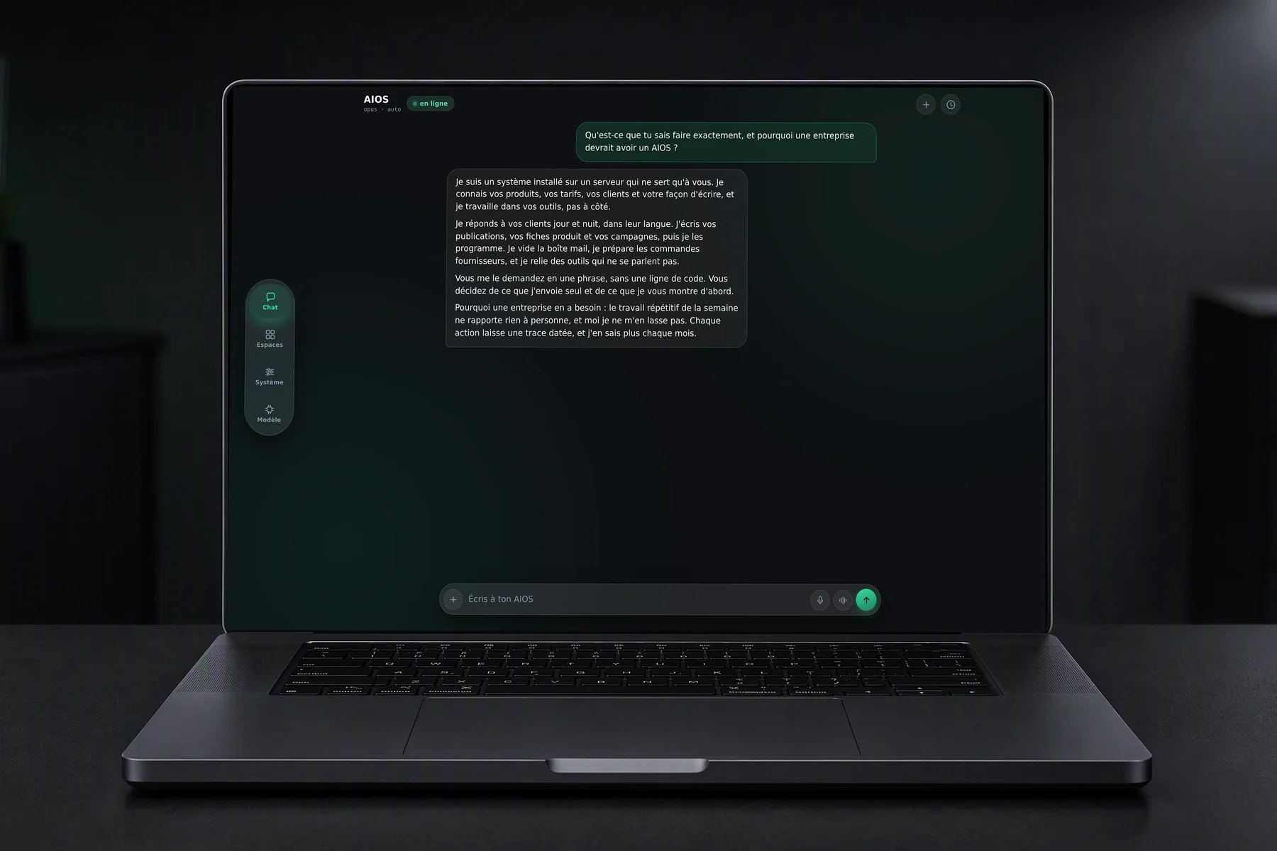 Un MacBook Pro noir posé sur un bureau sombre, l'AIOS ouvert à l'écran : on lui demande ce qu'il sait faire et pourquoi une entreprise devrait en avoir un, il répond.